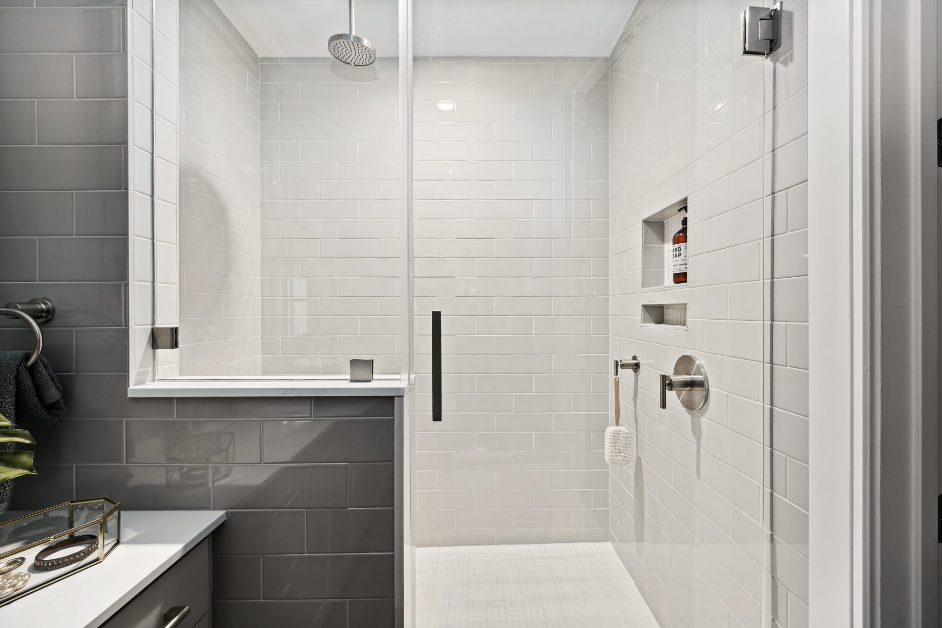 Interior view of a light grey tile shower with stainless steel overhead shower and glass door entryway
